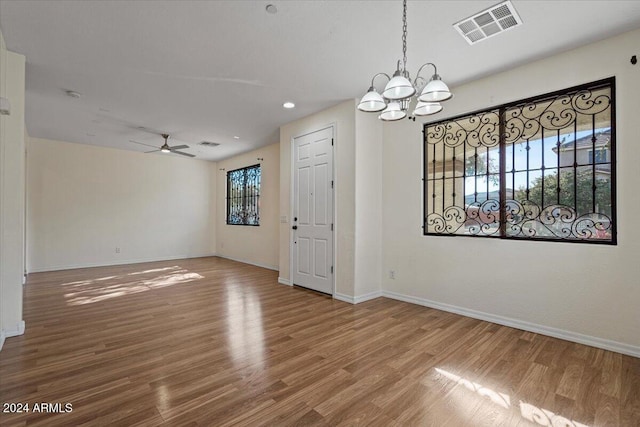 empty room with ceiling fan with notable chandelier and hardwood / wood-style floors