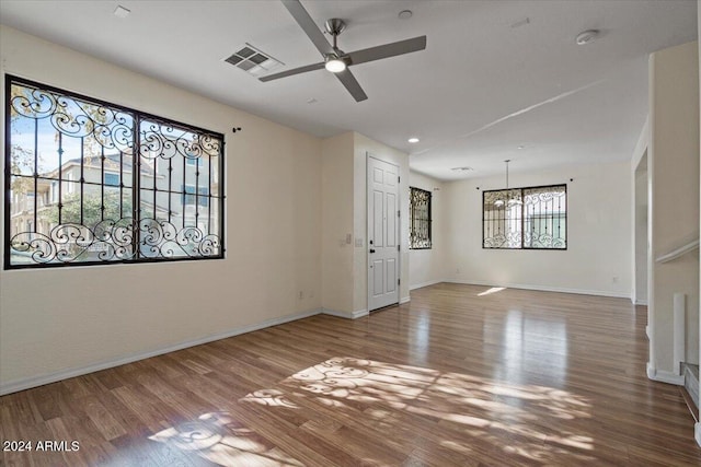 empty room featuring ceiling fan with notable chandelier and hardwood / wood-style flooring