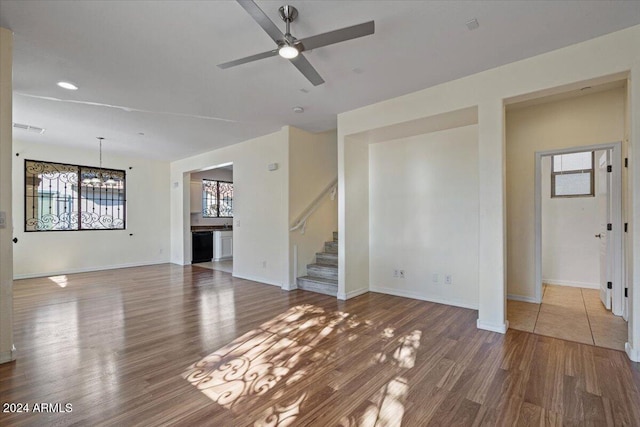 unfurnished living room featuring ceiling fan with notable chandelier and wood-type flooring