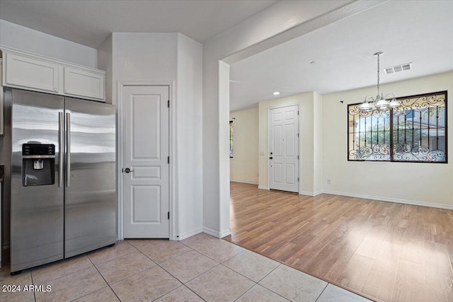 kitchen with stainless steel fridge with ice dispenser, light tile patterned floors, white cabinets, and decorative light fixtures