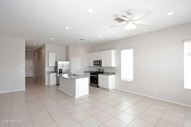kitchen featuring ceiling fan, appliances with stainless steel finishes, light stone countertops, white cabinets, and an island with sink
