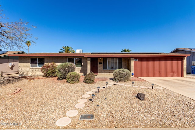 ranch-style house with driveway, roof mounted solar panels, and brick siding