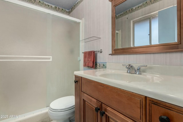 full bath with a stall shower, vanity, toilet, and wallpapered walls