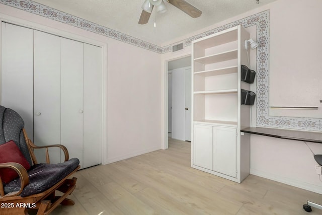 living area featuring visible vents, ceiling fan, a textured ceiling, and light wood finished floors