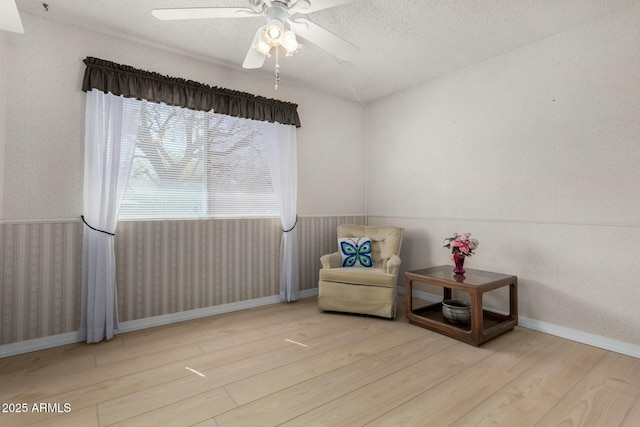 sitting room with wallpapered walls, baseboards, a ceiling fan, wood finished floors, and a textured ceiling