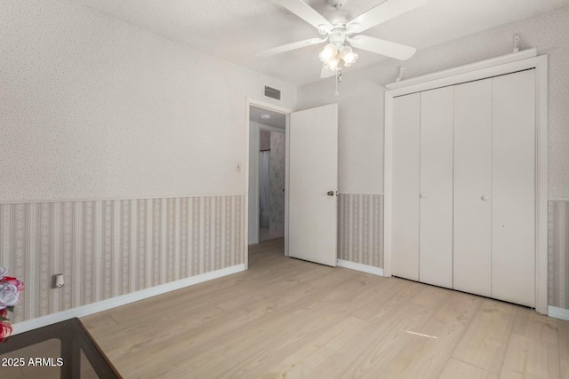 unfurnished bedroom with a closet, wood finished floors, visible vents, and wallpapered walls