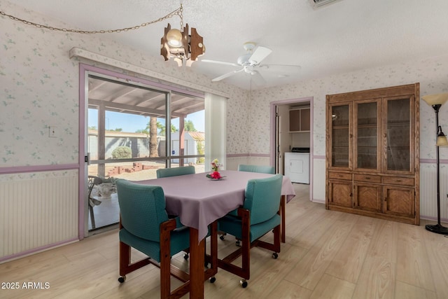 dining room featuring a notable chandelier, a wainscoted wall, light wood-type flooring, washer / clothes dryer, and wallpapered walls