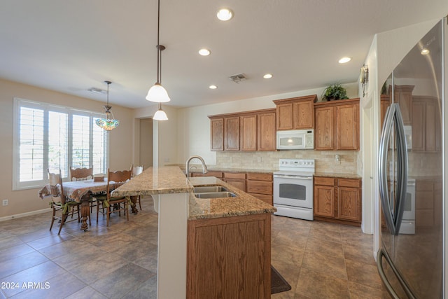 kitchen featuring a kitchen bar, white appliances, sink, decorative light fixtures, and an island with sink