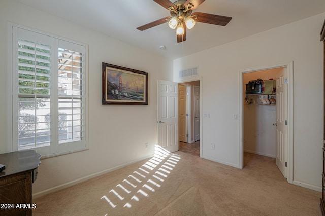 unfurnished bedroom with ceiling fan, a spacious closet, light carpet, and a closet