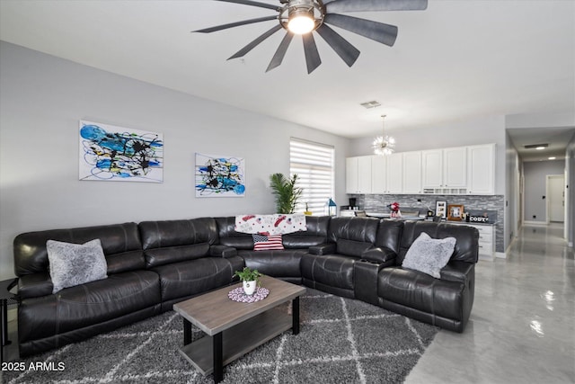 living room with ceiling fan with notable chandelier and concrete floors