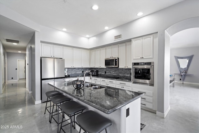 kitchen with sink, a breakfast bar area, white cabinetry, dark stone counters, and stainless steel appliances