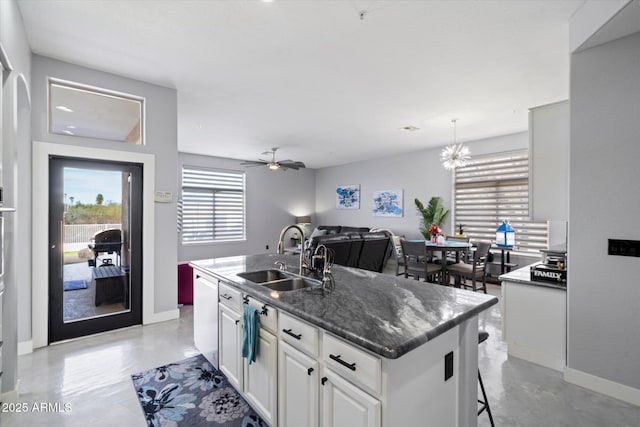 kitchen with sink, a kitchen island with sink, white dishwasher, white cabinets, and decorative light fixtures