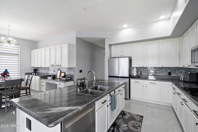 kitchen with appliances with stainless steel finishes, a center island with sink, white cabinets, and decorative light fixtures