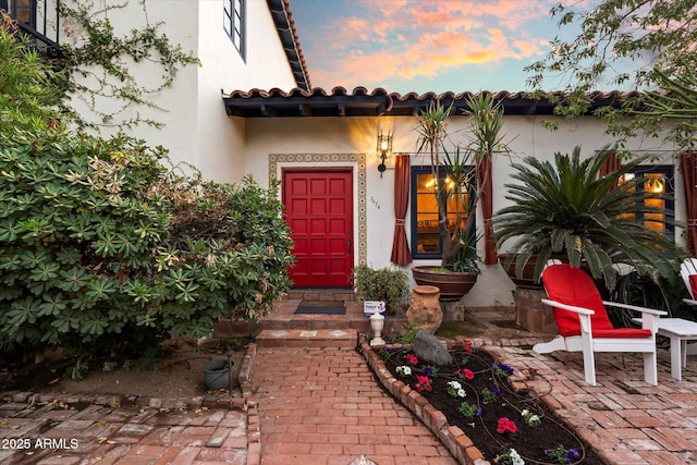 view of exterior entry with stucco siding and a tiled roof