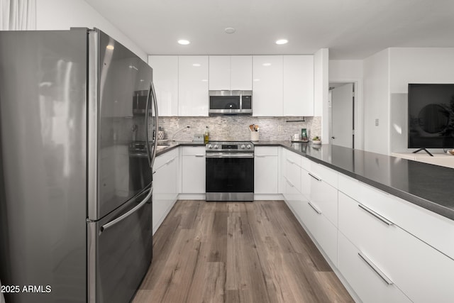 kitchen featuring modern cabinets, dark wood-style flooring, dark countertops, white cabinets, and appliances with stainless steel finishes