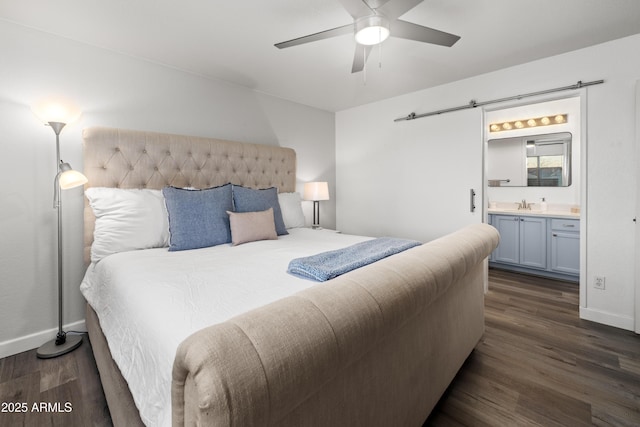 bedroom featuring dark wood-type flooring, a barn door, ensuite bath, and baseboards