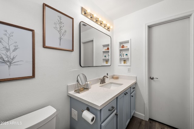 half bath featuring wood finished floors, toilet, and vanity