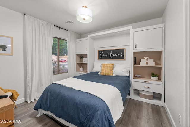 bedroom with wood finished floors, visible vents, and baseboards