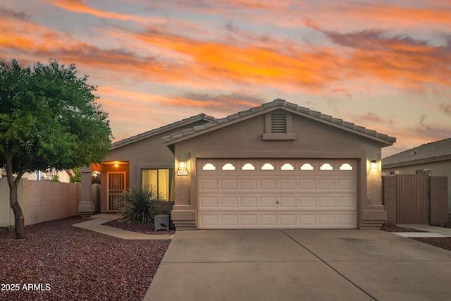 view of front facade with driveway, stucco siding, an attached garage, and fence