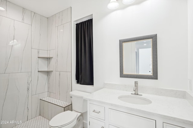 bathroom featuring a tile shower, vanity, and toilet