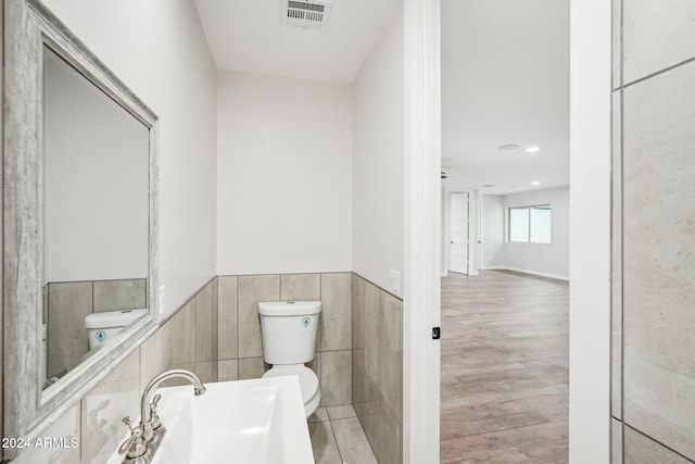 bathroom featuring tile walls, hardwood / wood-style flooring, toilet, and sink