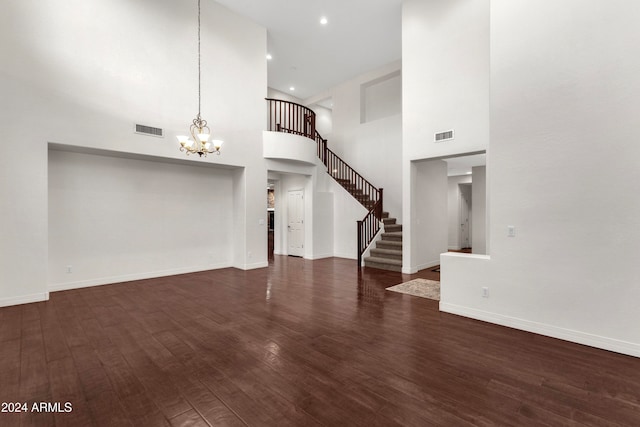 unfurnished living room featuring a towering ceiling, dark hardwood / wood-style floors, and a notable chandelier