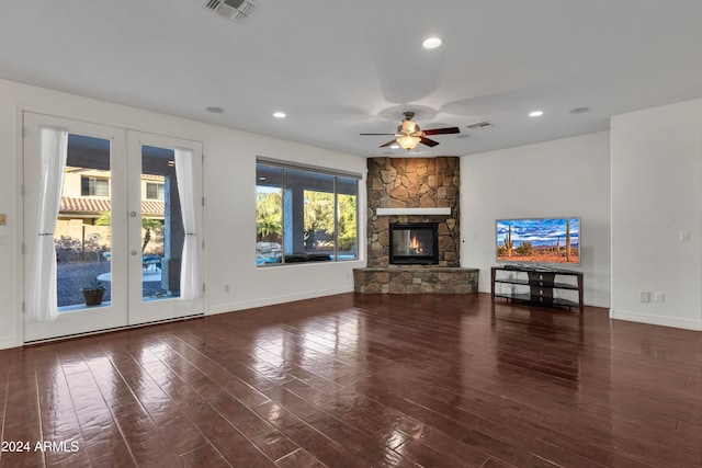 unfurnished living room with ceiling fan, a stone fireplace, dark hardwood / wood-style flooring, and french doors