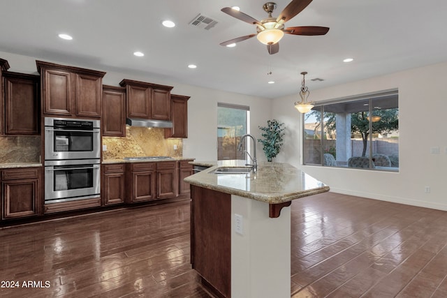 kitchen with dark wood-type flooring, sink, an island with sink, tasteful backsplash, and stainless steel appliances