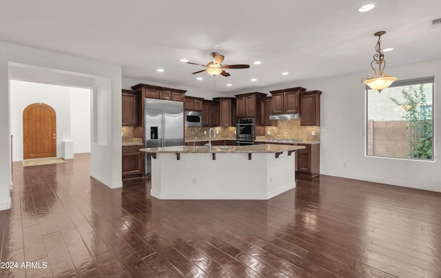 kitchen featuring built in appliances, a breakfast bar, pendant lighting, and dark hardwood / wood-style flooring