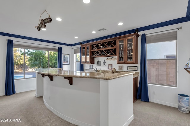 kitchen featuring a breakfast bar, light carpet, crown molding, and light stone counters