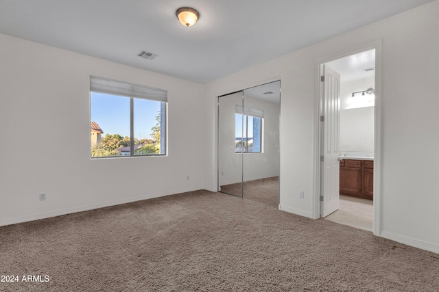 unfurnished bedroom with a closet, light colored carpet, and ensuite bath