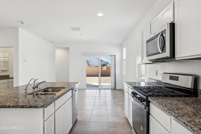 kitchen featuring sink, appliances with stainless steel finishes, white cabinets, a center island with sink, and dark stone counters