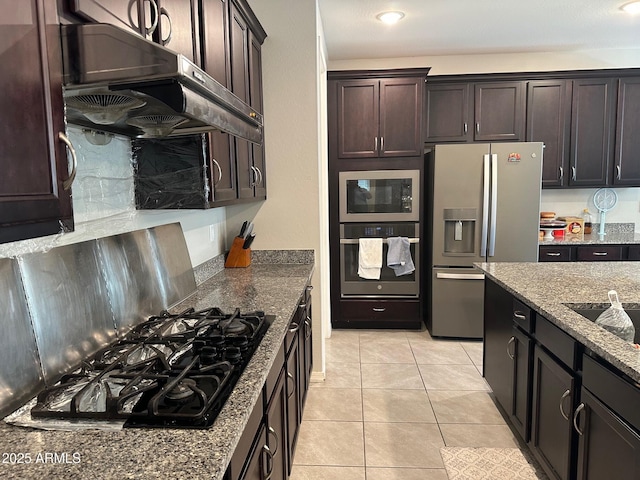 15301 W Moreland St, Goodyear, AZ 85338 - kitchen featuring under cabinet range hood, light tile patterned floors, dark brown cabinetry, dark stone counters, and appliances with stainless steel finishes