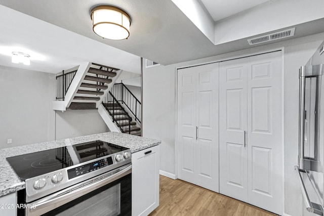 kitchen with stainless steel electric range, white cabinets, light wood-type flooring, and light stone countertops