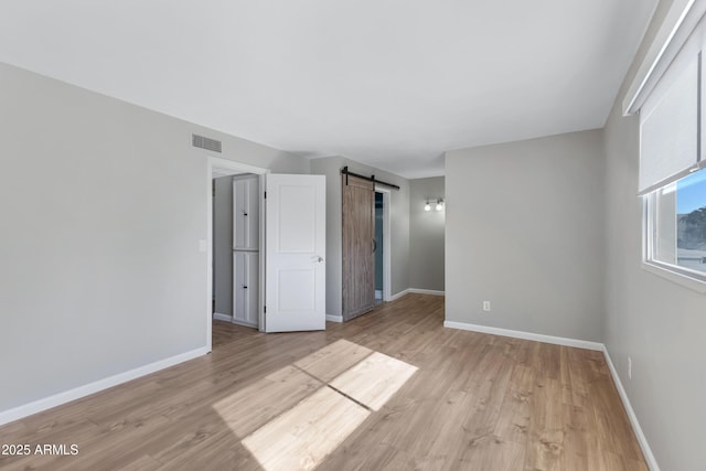 unfurnished bedroom with a barn door and light hardwood / wood-style floors