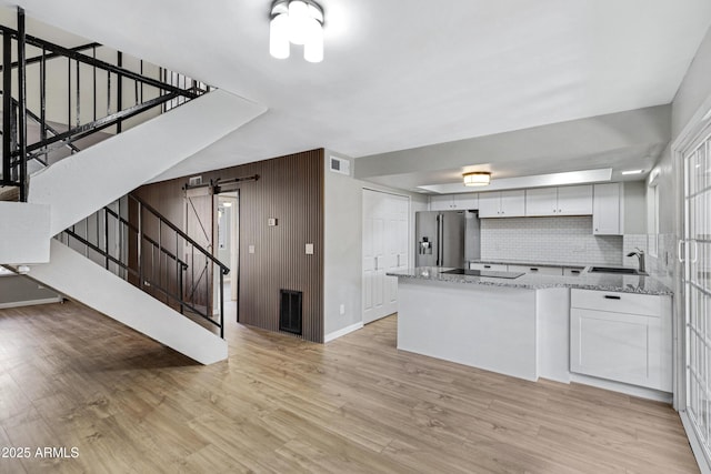 kitchen featuring white cabinets, decorative backsplash, a barn door, light stone countertops, and stainless steel fridge