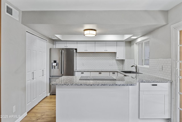 kitchen featuring sink, white cabinets, light stone counters, kitchen peninsula, and stainless steel fridge