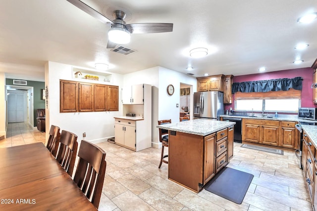 kitchen with light stone countertops, appliances with stainless steel finishes, a kitchen bar, a center island, and ceiling fan