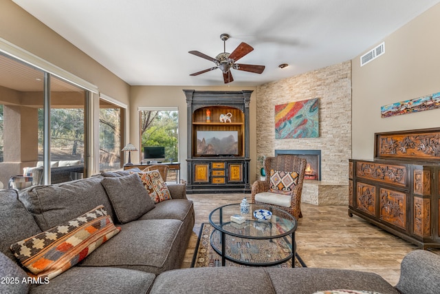 living room with a stone fireplace, light hardwood / wood-style flooring, and ceiling fan