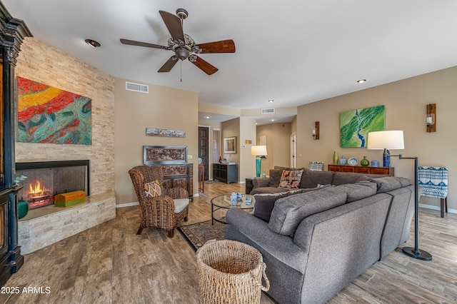 living room featuring wood-type flooring, a stone fireplace, and ceiling fan