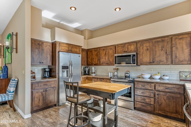 kitchen featuring tasteful backsplash, appliances with stainless steel finishes, light stone counters, and light wood-type flooring