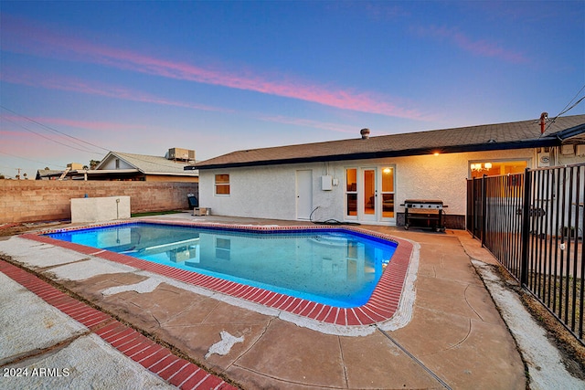 pool at dusk featuring french doors and a patio