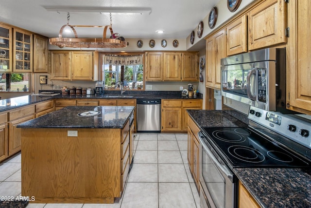 kitchen featuring a center island, stainless steel appliances, dark stone counters, sink, and light tile patterned floors