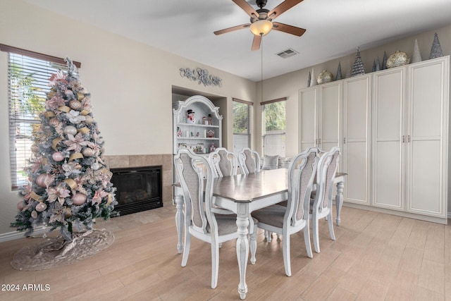 dining room with a tile fireplace, light hardwood / wood-style floors, and ceiling fan