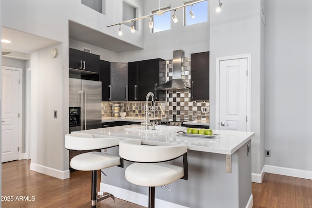 15221 N Clubgate Dr Unit 2059, Scottsdale, AZ 85254 - kitchen featuring wall chimney range hood, stainless steel fridge with ice dispenser, dark cabinetry, a high ceiling, and tasteful backsplash