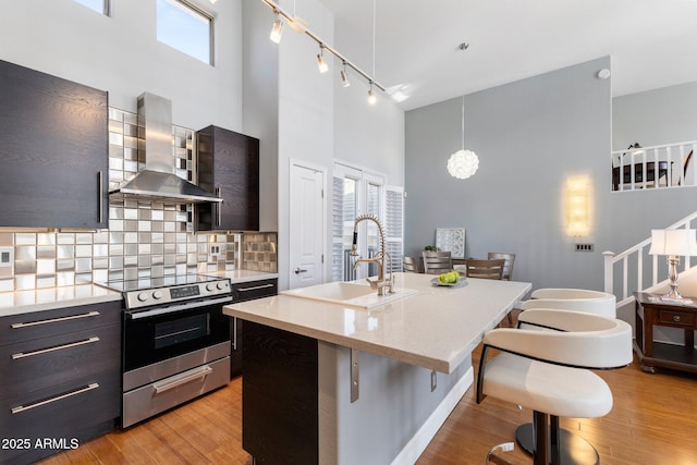 15221 N Clubgate Dr Unit 2059, Scottsdale, AZ 85254 - kitchen featuring stainless steel range with electric cooktop, a sink, wall chimney range hood, a towering ceiling, and a breakfast bar area