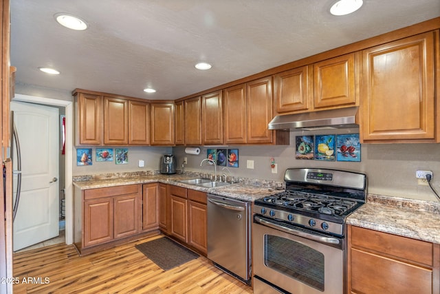 kitchen with sink, stainless steel appliances, light wood-type flooring, and light stone countertops