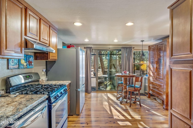 kitchen featuring light stone counters, stainless steel appliances, light hardwood / wood-style floors, and hanging light fixtures