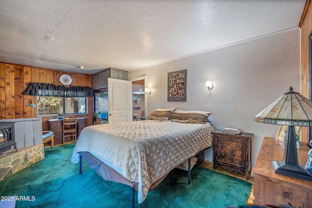 bedroom featuring a textured ceiling, wood walls, a wood stove, and dark carpet