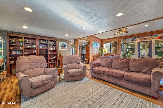 living room featuring a textured ceiling, ceiling fan, light wood-type flooring, and wooden walls